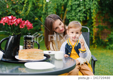 Happy Mother Watching Son Eating Cake In Garden Happy Mother Watching Son Eating Cake In Garden 141720480