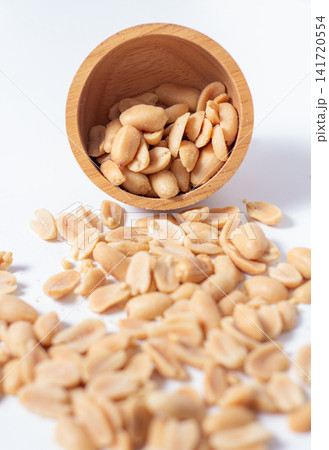 Peanuts in a wooden cup rest on a white background, creating a warm and rustic food-themed scene. Peanuts in a wooden cup rest on a white background, creating a warm and rustic food-themed scene. 141720554