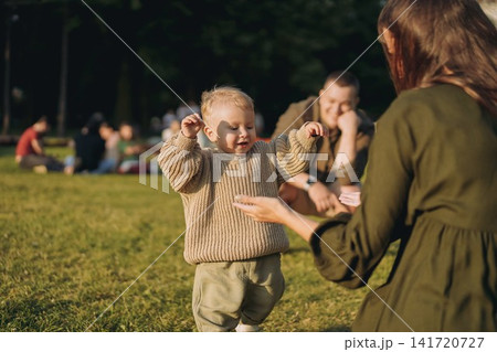 young parents with baby son learning to walk in the park young parents with baby son learning to walk in the park 141720727