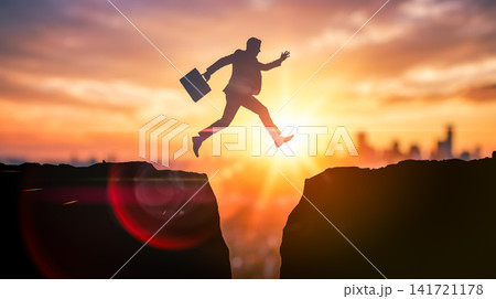 Corporate worker silhouette carrying briefcase leaping across dangerous gap between steep mountain cliffs with modern city skyline during vibrant golden sunset background Corporate worker silhouette carrying briefcase leaping across dangerous gap between steep mountain cliffs with modern city skyline during vibrant golden sunset background 141721178