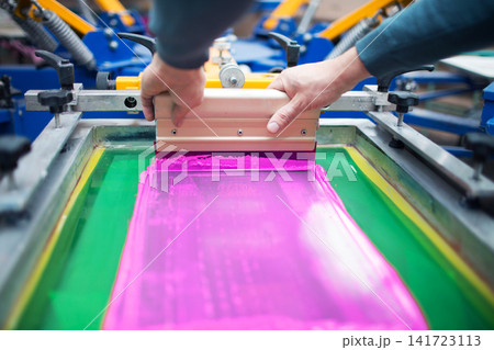 Silk screen printing technology. Serigraphy and Color paints applying to fabric. Plastisol paint and squeegee in hands Silk screen printing technology. Serigraphy and Color paints applying to fabric. Plastisol paint and squeegee in hands 141723113