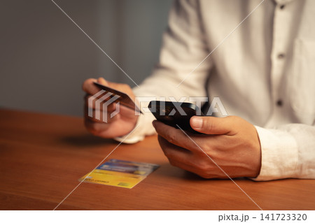 Adult man uses a smartphone and credit card for online shopping and payment. This e-commerce technology allows secure mobile banking, finance, and business transactions over the internet. 141723320