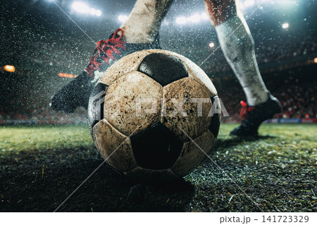 Weathered soccer ball dominating foreground as football player moves across rain-soaked turf Weathered soccer ball dominating foreground as football player moves across rain-soaked turf 141723329