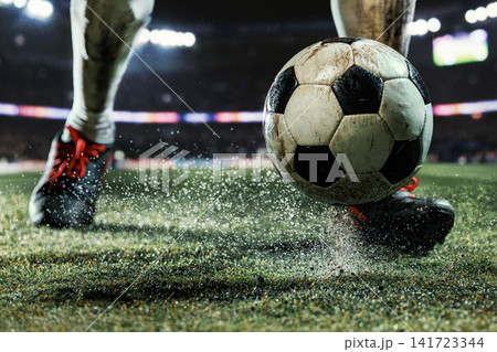 Close-up soccer ball rolling between player boots on wet illuminated football pitch 141723344