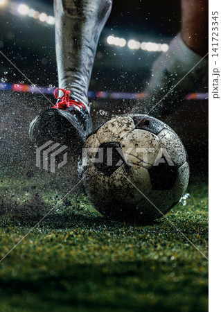 Mud-covered cleat controlling weathered football as dirt sprays across textured stadium turf 141723345