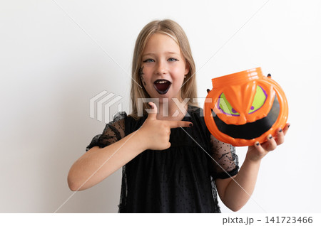 Girl in witch costume pointing at pumpkin candy bucket on white background Girl in witch costume pointing at pumpkin candy bucket on white background 141723466