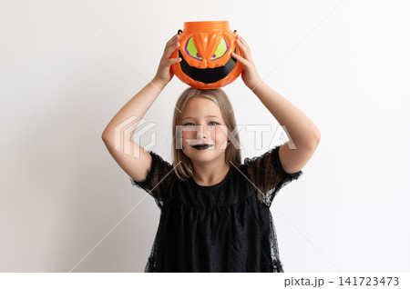 Girl child in witch costume holding pumpkin bucket on head on white background Girl child in witch costume holding pumpkin bucket on head on white background 141723473