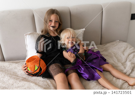 Two sisters in witch costumes hugging and laughing on bed with pumpkin bucket Two sisters in witch costumes hugging and laughing on bed with pumpkin bucket 141723501