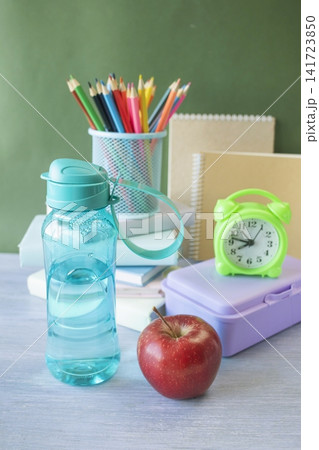 School supplies and healthy lunch on the table for studying. Alarm clock, textbooks, colored pencils and bottle of water and lunch box, back to school concept. School supplies and healthy lunch on the table for studying. Alarm clock, textbooks, colored pencils and bottle of water and lunch box, back to school concept. 141723850