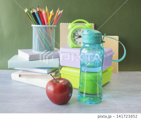 School supplies and healthy lunch on the table for studying. Alarm clock, textbooks, colored pencils and bottle of water and lunch box, back to school concept. 141723852