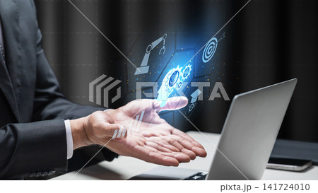 Businessman gesturing toward a glowing holographic interface depicting AI, automation, and business target icons next to a laptop. AI Education concept Businessman gesturing toward a glowing holographic interface depicting AI, automation, and business target icons next to a laptop. AI Education concept 141724010