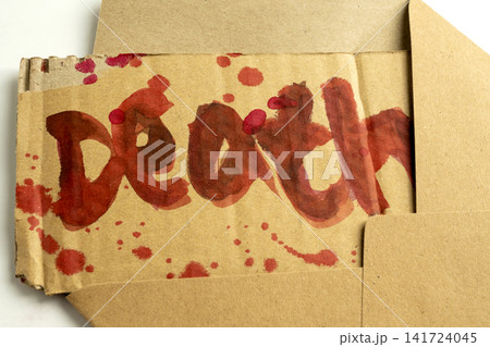 A threatening message reading Death written in red blood on a piece of cardboard, emerging from a brown paper envelope, suggesting a crime, stalker, or horror theme. Concept of Halloween 141724045
