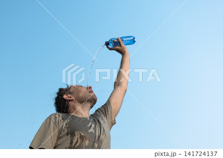 Man pouring water on himself from a plastic water bottle outdoors, illustrating how to cope with extreme heat in European cities. Man pouring water on himself from a plastic water bottle outdoors, illustrating how to cope with extreme heat in European cities. 141724137