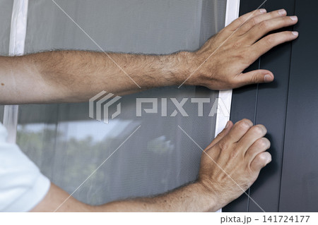 White magnetic mosquito screen into the frame of balcony door, illustrating precise attachment in practical home maintenance. White magnetic mosquito screen into the frame of balcony door, illustrating precise attachment in practical home maintenance. 141724177