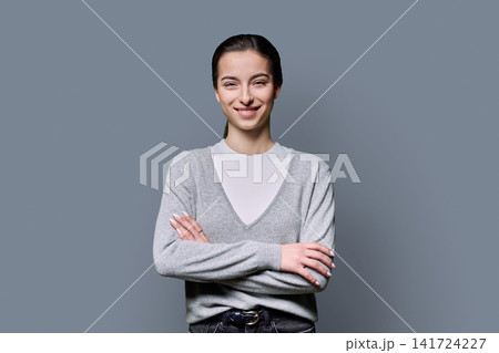 Portrait of a confident 18-year-old young woman with crossed arms on grey background Portrait of a confident 18-year-old young woman with crossed arms on grey background 141724227