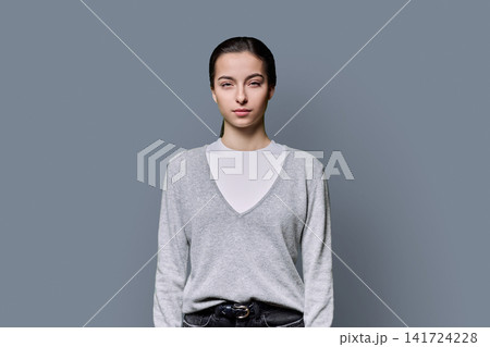 Portrait of a serious 18-year-old young woman on grey studio background 141724228