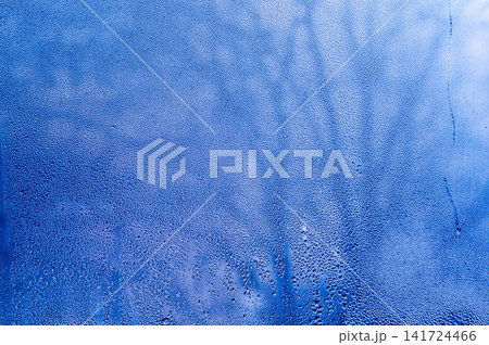 Condensation creates frosty blue texture on clear glass pane. Cold humidity layer displays abstract frozen mist during winter season for creative project. Light condensation offers fresh backdrop Condensation creates frosty blue texture on clear glass pane. Cold humidity layer displays abstract frozen mist during winter season for creative project. Light condensation offers fresh backdrop 141724466