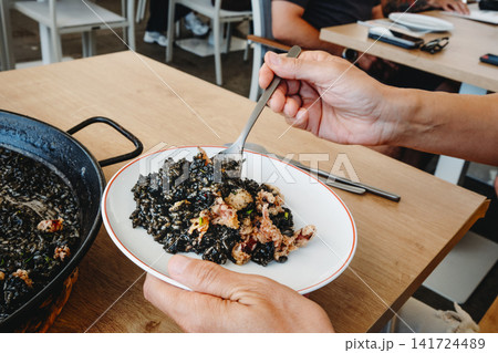 man serving spanish arros negre from paella 141724489