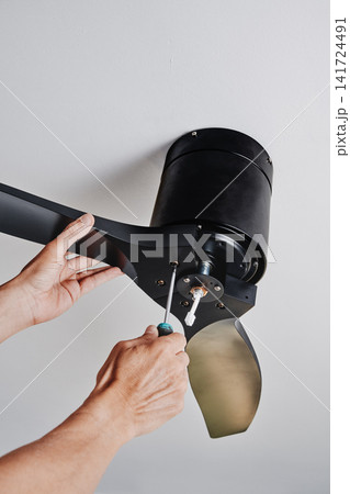 man securing a ceiling fan while installing it man securing a ceiling fan while installing it 141724491
