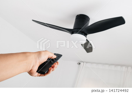 man operating a ceiling fan with remote control 141724492