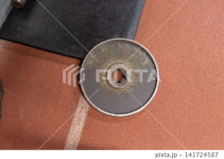 Old weight plate on a gym floor near training equipment in a sports facility during a workout session Old weight plate on a gym floor near training equipment in a sports facility during a workout session 141724587