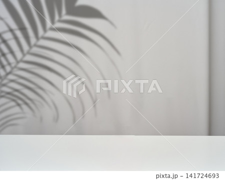 A white, empty tabletop with a soft palm branch shadow against a gray wall. A white, empty tabletop with a soft palm branch shadow against a gray wall. 141724693