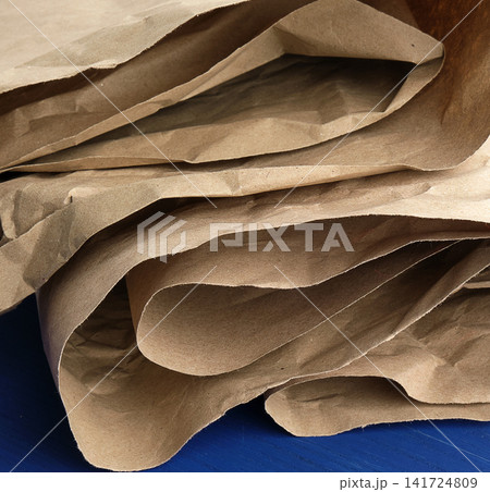 Crumpled brown craft paper in folds and bends lies on a blue wooden surface Crumpled brown craft paper in folds and bends lies on a blue wooden surface 141724809