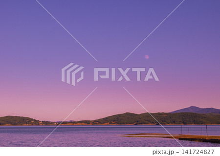 Scenic tranquil landscape of Plastiras lake during purple dusk sunset with full moon in sky over mountain shore in Thessaly Greece for wallpaper background photo Scenic tranquil landscape of Plastiras lake during purple dusk sunset with full moon in sky over mountain shore in Thessaly Greece for wallpaper background photo 141724827