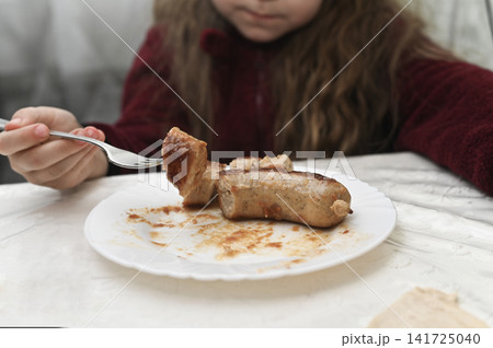 little girl eating cooked sausage pieces on plate, using fork, little girl eating cooked sausage pieces on plate, using fork, 141725040