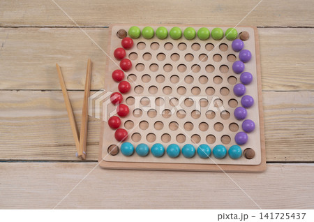 Educational game with colorful wooden beads lies on light wooden background table. Montessori learning set helps children develop fine motor skills. Interactive game promotes early child training. Educational game with colorful wooden beads lies on light wooden background table. Montessori learning set helps children develop fine motor skills. Interactive game promotes early child training. 141725437