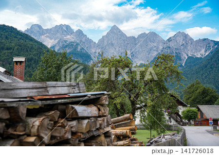 Stacked firewood and village houses in Kranjska Gora, Slovenia, with the rocky Julian Alps in the background, showing everyday alpine life and strong sense of place Stacked firewood and village houses in Kranjska Gora, Slovenia, with the rocky Julian Alps in the background, showing everyday alpine life and strong sense of place 141726018