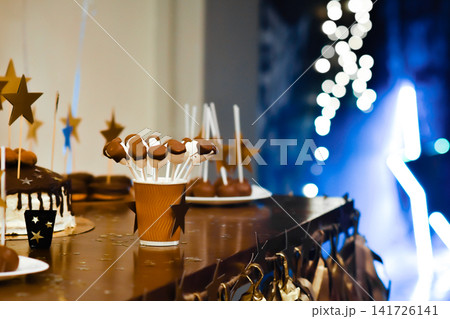 Cake pops stand in paper cup on festive candy bar table during birthday party. Delicious chocolate treats provide sweet snack for holiday event guests. Yummy pops decorate dessert buffet table. Cake pops stand in paper cup on festive candy bar table during birthday party. Delicious chocolate treats provide sweet snack for holiday event guests. Yummy pops decorate dessert buffet table. 141726141