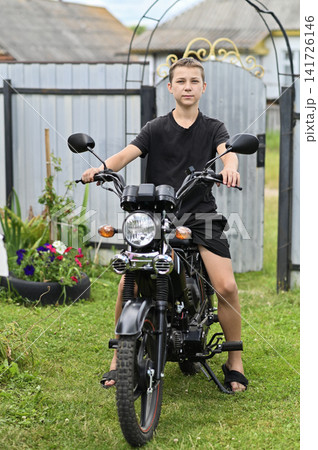 Boy sitting on moped in green backyard near flowers. Boy sitting on moped in green backyard near flowers. 141726146