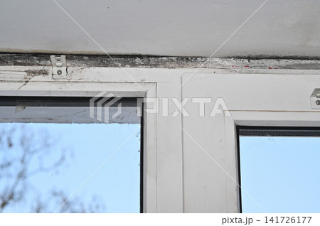 Close-up view of window with visible mold and dirt on frame. Window frame showing signs of mold and dirt accumulation, with detailed view of affected areas, revealing moisture damage. 141726177