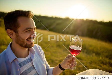 Smiling man holding glass of rose wine against golden countryside landscape 141726643