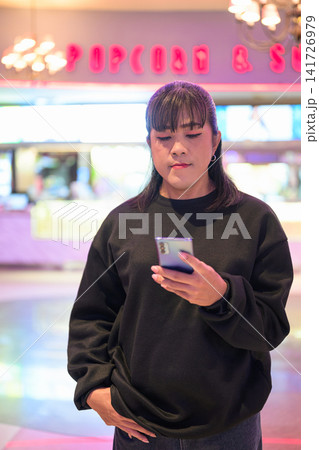Asian Person Using Mobile Phone in Movie Theater Foyer 141726979