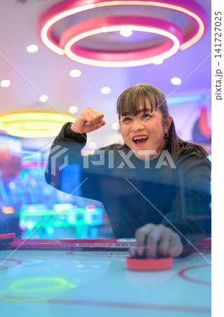 Excited Woman Celebrating Victory at Air Hockey Table 141727025