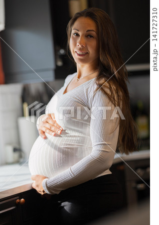 Pregnant woman smiling warmly in a kitchen with soft natural light Pregnant woman smiling warmly in a kitchen with soft natural light 141727310