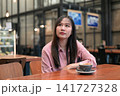 Thoughtful Asian Woman Looking Up while Sitting in a Cafe with Coffee 141727328