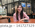 Happy Asian Woman Smiling and Looking Up in a Cafe with a Cup of Coffee 141727329