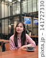 Thoughtful Asian Woman Looking Up while Sitting in a Cafe with Coffee 141727330