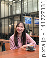 Happy Asian Woman Smiling and Looking Up in a Cafe with a Cup of Coffee 141727331