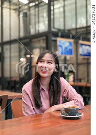 Happy Asian Woman Smiling and Looking Up in a Cafe with a Cup of Coffee 141727331