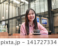 Smiling Asian Woman Sitting with a Cup of Coffee in a Modern Cafe 141727334