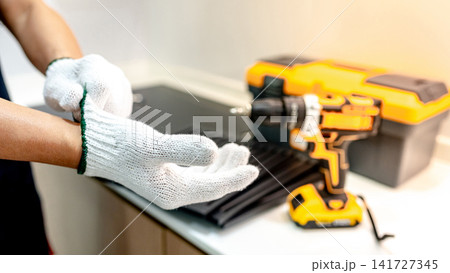 Male hand of maintenance worker putting on protective gloves near work tools in the kitchen 141727345