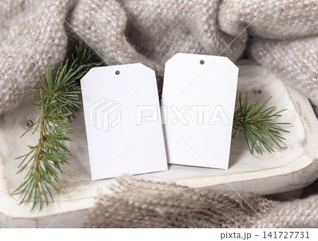 Two vertical gift tag mockup near beige knitted blanket and fir branches. Rustic Christmas packaging 141727731