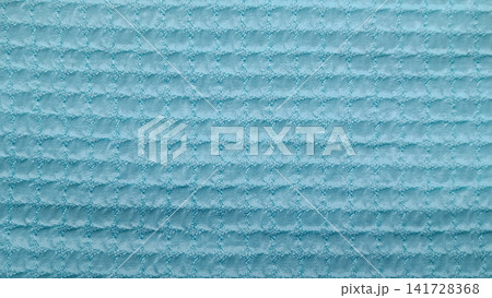 Close up of pastel blue waffle weave fabric with a soft, raised square grid design creating a three dimensional, pillowy surface. Close up of pastel blue waffle weave fabric with a soft, raised square grid design creating a three dimensional, pillowy surface. 141728368