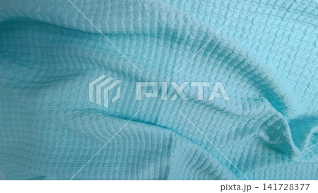 Abstract close up of quilted light blue fabric with a stitched square grid creating a raised, tactile surface. Abstract close up of quilted light blue fabric with a stitched square grid creating a raised, tactile surface. 141728377