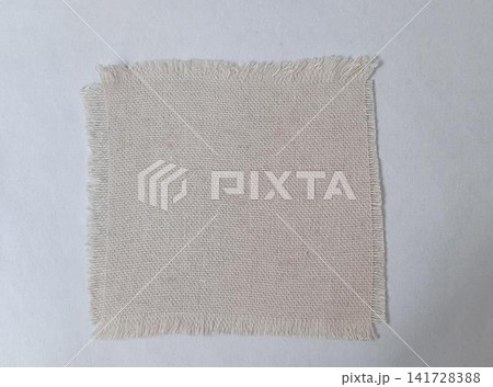 A square swatch of light beige, loose coarse woven fabric with fringed edges, placed on a plain white background. 141728388