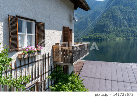 Old house white wall facade. Rustic Alpine Window with Brown Wooden Shutters, White Lace Curtains and Pink Blooming Flowers 141728672